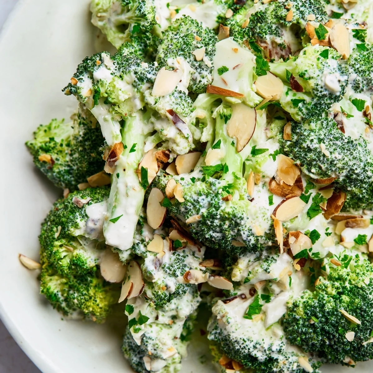 Bright green broccoli florets tossed with creamy garlic-Parmesan dressing in a ceramic bowl, garnished with fresh parsley.