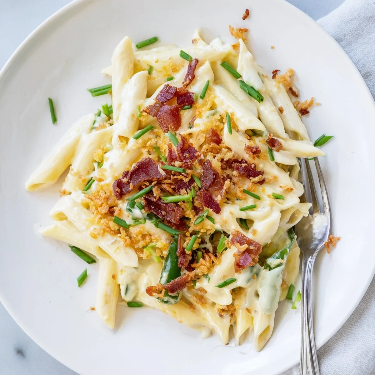 Served warm in a rustic white bowl, this decadent jalapeño popper pasta offers a vibrant contrast of green peppers and golden bacon, perfect for an easy weeknight dinner.