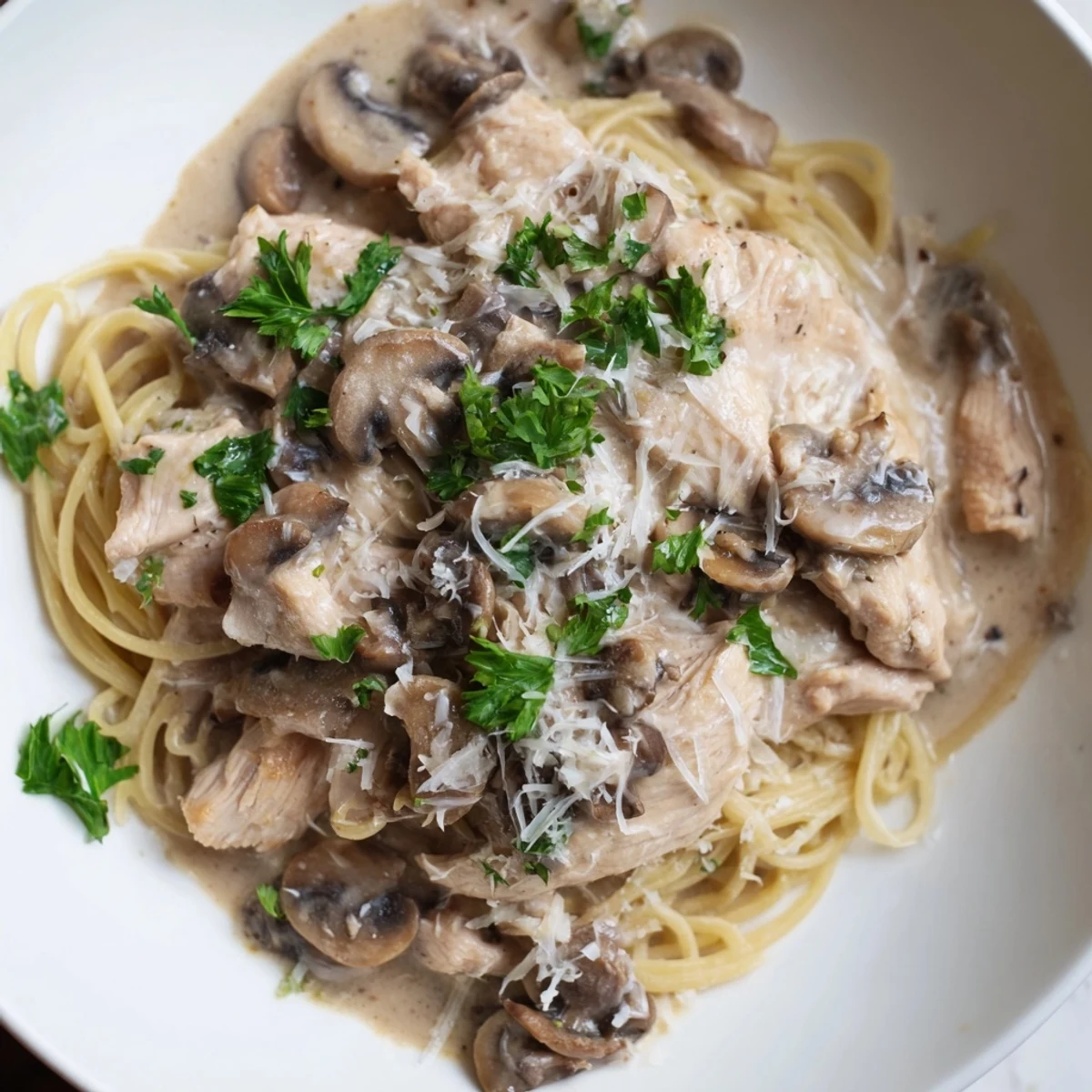 A skillet of Creamy Mushroom Chicken Spaghettini reveals golden seared chicken strips nestled in silky sauce with sautéed mushrooms and fresh thyme.  