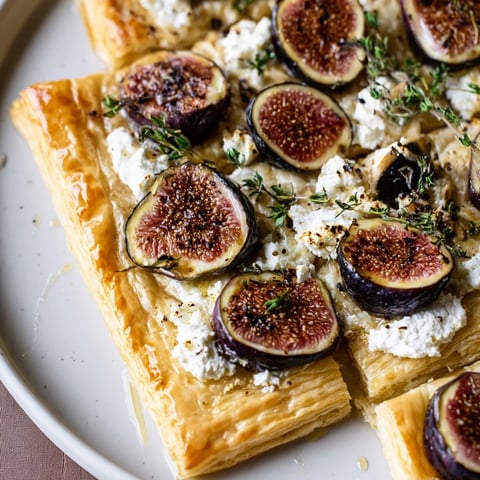 Golden, puffed puff pastry truffle pizza showcasing figs, goat cheese, with a drizzle of honey.