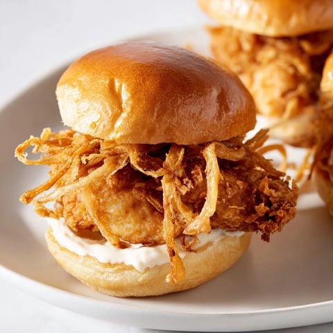 Golden fried chicken thighs and crunchy onion strings stacked on a toasted brioche bun with creamy garlic aioli.
