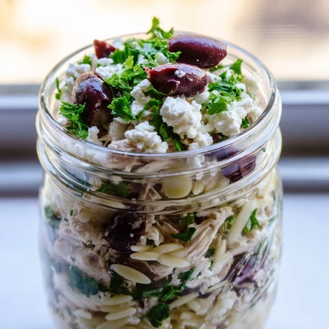 Freshly prepared Greek Pasta Chicken Salad Jars layered with orzo, diced chicken, cherry tomatoes, and cucumber, ready for a healthy grab-and-go Mediterranean lunch.