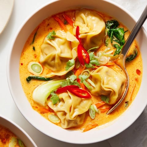 A close-up view of steaming Red Curry Wonton Soup in a ceramic bowl, showcasing tender wontons and vibrant greens in rich, aromatic broth.