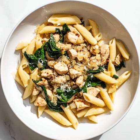A steaming bowl of One-Pot Spinach and Chicken Pasta, rich with savory broth and perfectly cooked pasta.