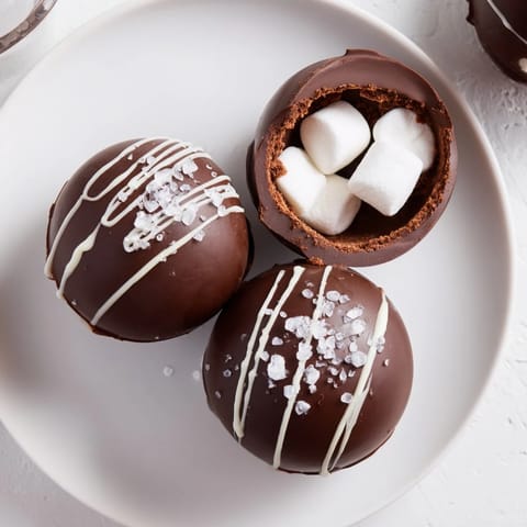 Homemade Hot Chocolate Bombs decorated with white chocolate drizzle and colorful sprinkles on a rustic wooden table.