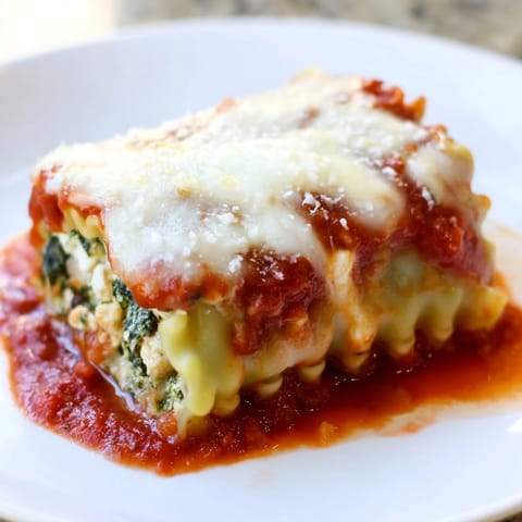 Freshly baked Chicken and Spinach Lasagna Rolls reveal creamy ricotta and spinach filling, served on a white plate with a side salad.