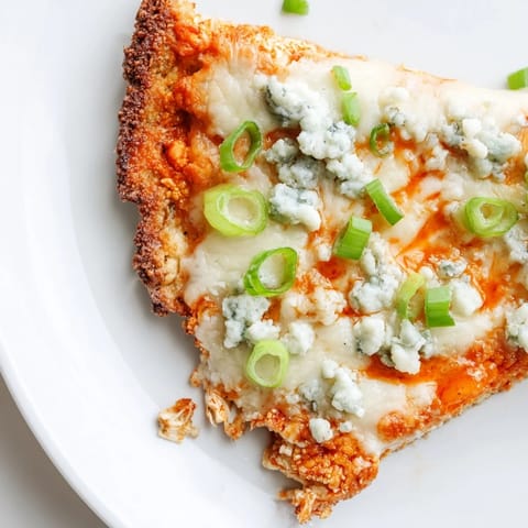 A close-up of Buffalo Cauliflower Pizza slices, with melted cheese and celery garnish on a rustic wooden serving board.  