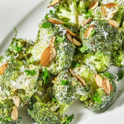 A close-up of Garlic Parmesan Broccoli Salad with cherry tomatoes, red onion, and slivered almonds, served as a fresh side.