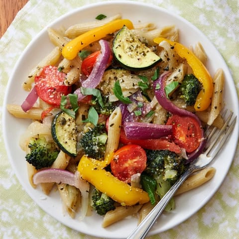 Twirled forkful of colorful Pasta Primavera with zucchini, bell peppers, and cherry tomatoes over a rustic white plate.