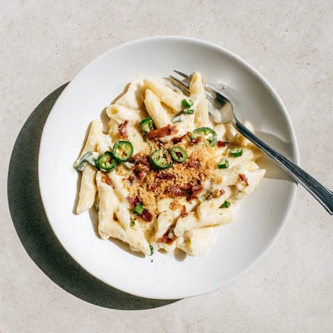 A steaming bowl of creamy jalapeño popper pasta, garnished with toasted panko breadcrumbs and fresh chives, showcases melted cheese clinging to every spiral of pasta.  