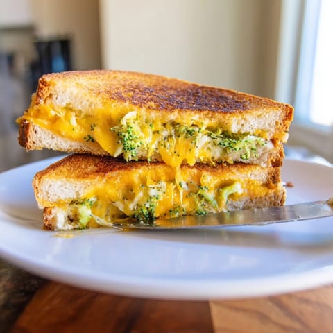 Roasted Broccoli & Cheddar Grilled Cheese sandwich resting on a white plate, featuring crispy bread and gooey cheese pull with vibrant green florets.
