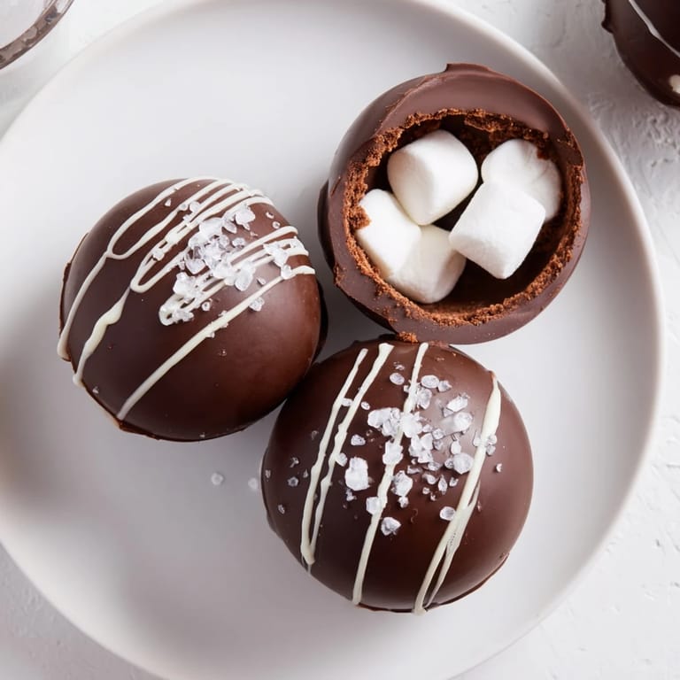 Homemade Hot Chocolate Bombs decorated with white chocolate drizzle and colorful sprinkles on a rustic wooden table.