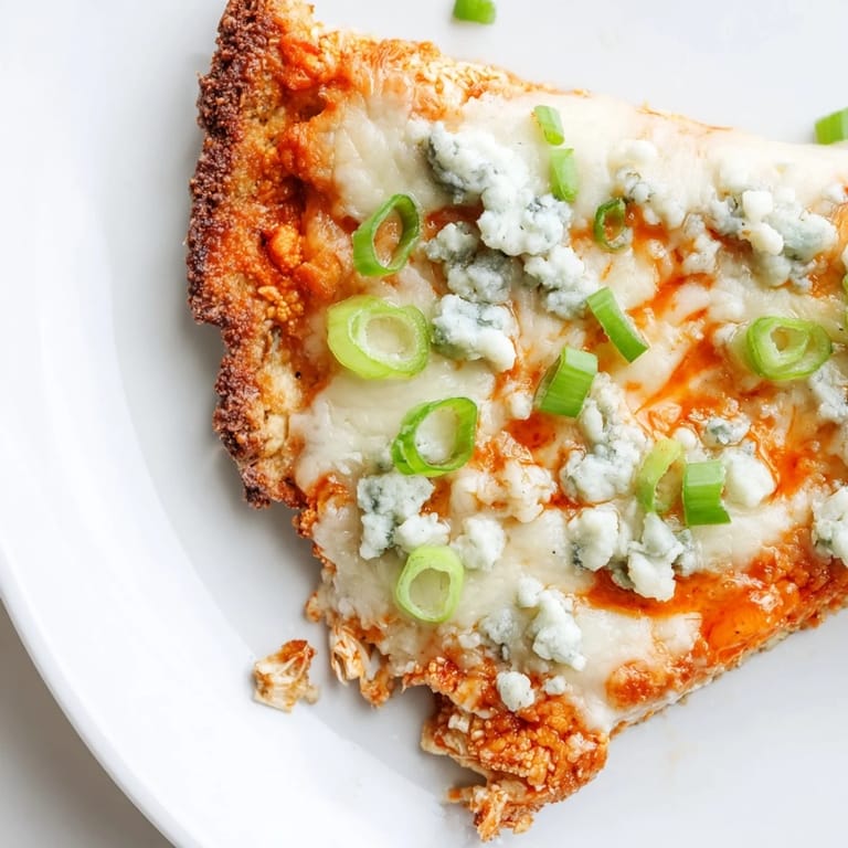 A close-up of Buffalo Cauliflower Pizza slices, with melted cheese and celery garnish on a rustic wooden serving board.  