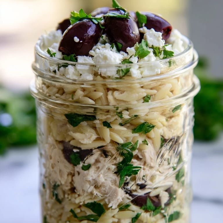 Clear glass mason jars displaying colorful layers of Greek-inspired salad with red bell peppers, red onion, parsley, and creamy feta for an easy weekday meal.