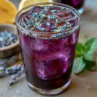 Vibrant purple lavender lemonade refresher with fresh lemon slices and sprigs of lavender, offering a floral citrus aroma and cooling refreshment.